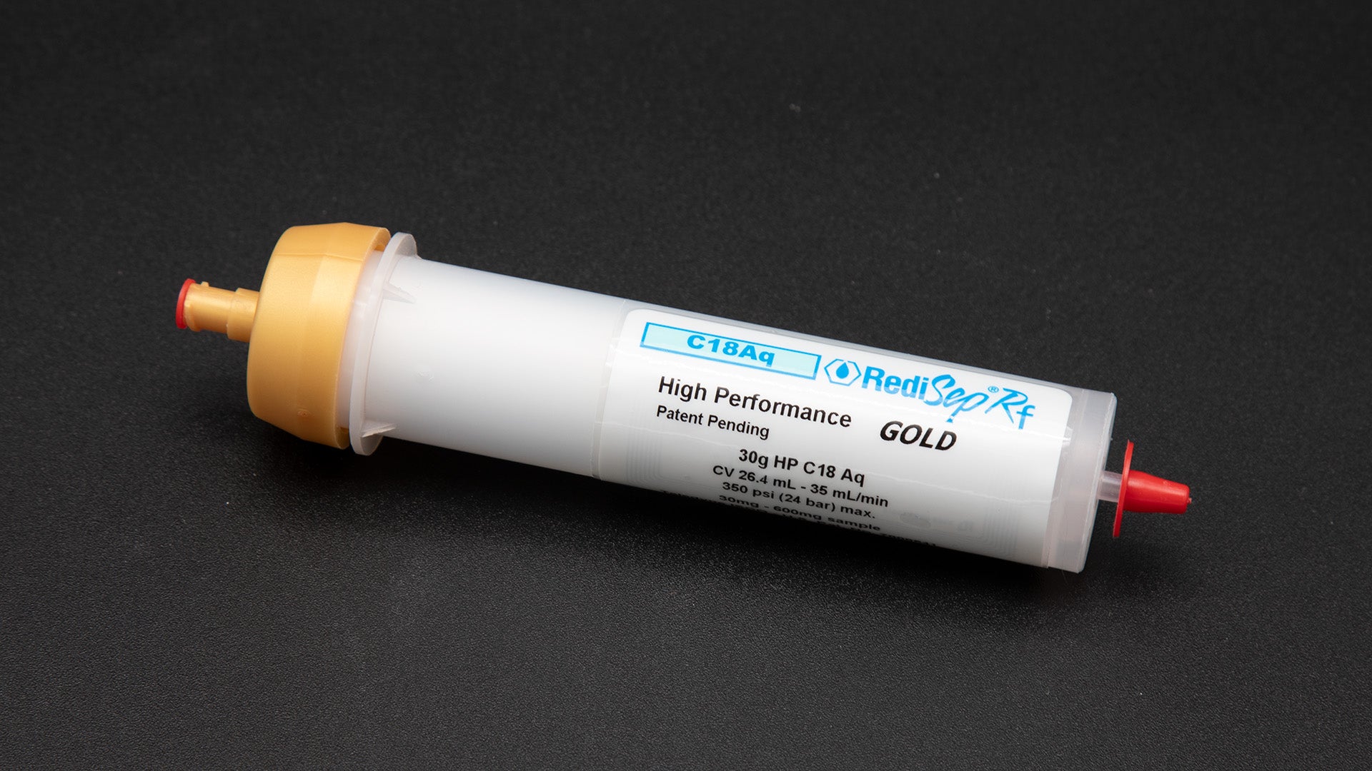 A small white tube with gold and red caps displayed on a black background, creating a striking visual contrast between the two elements.