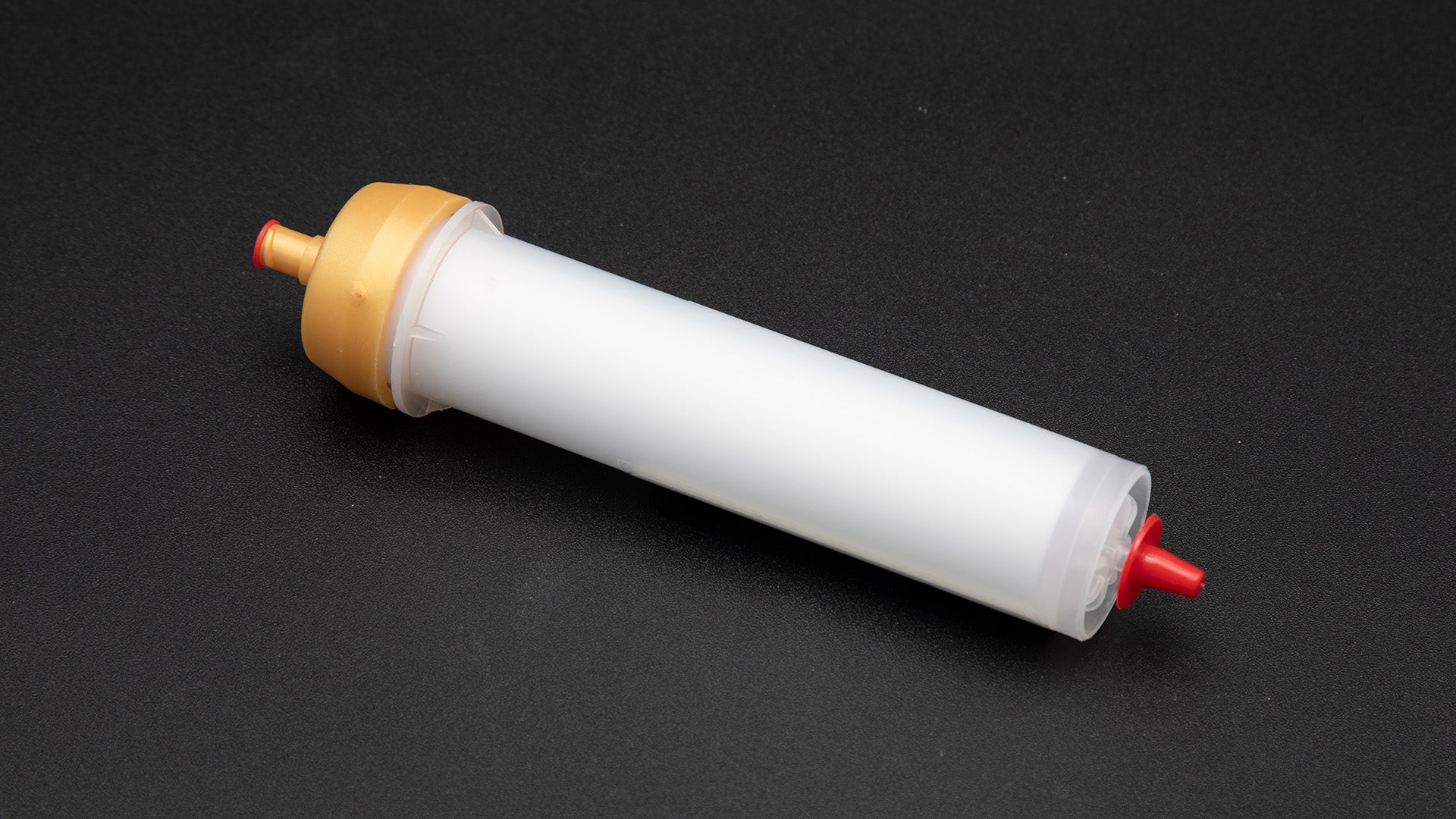 A small white tube with gold and red caps displayed on a black background, creating a striking visual contrast between the two elements.