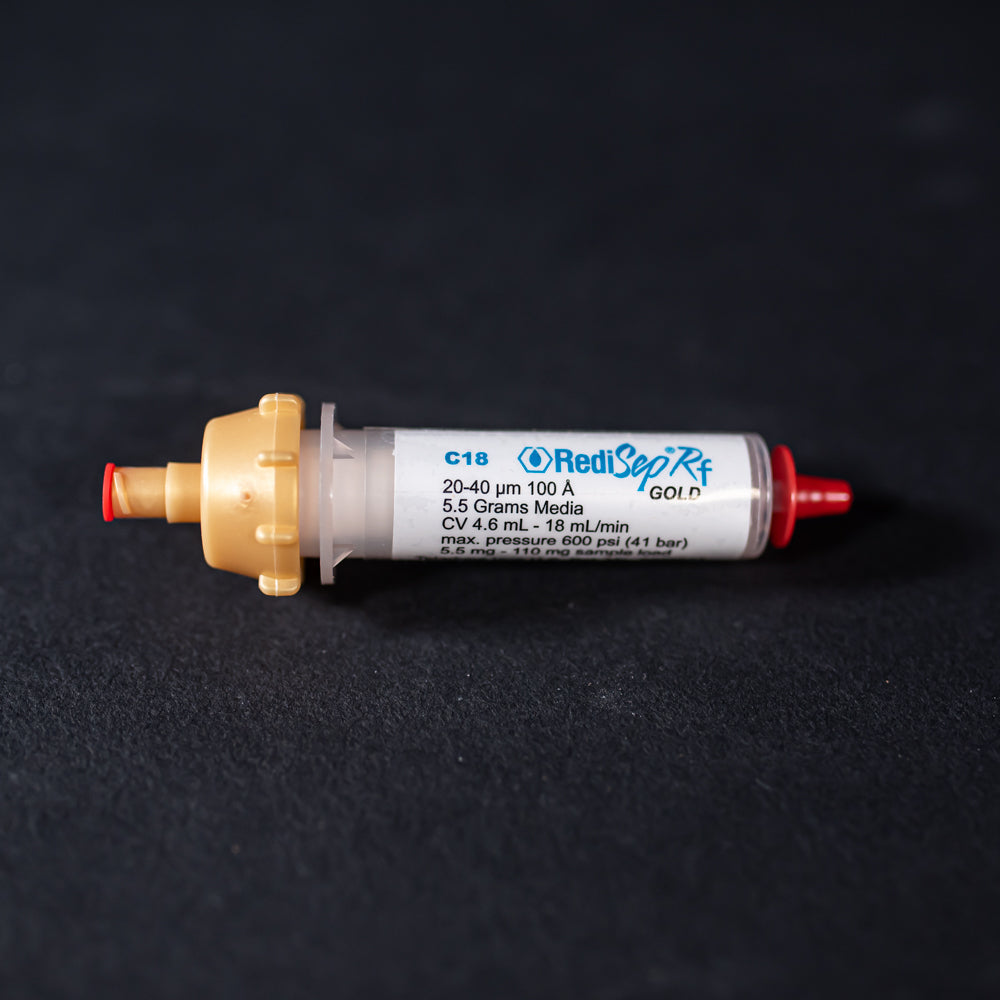 A small white tube with gold and red caps displayed on a black background, creating a striking visual contrast between the two elements.