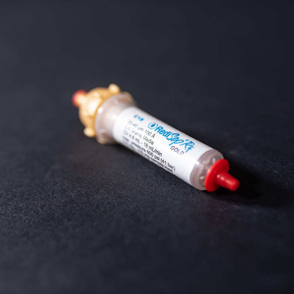 A small white tube with gold and red caps displayed on a black background, creating a striking visual contrast between the two elements.