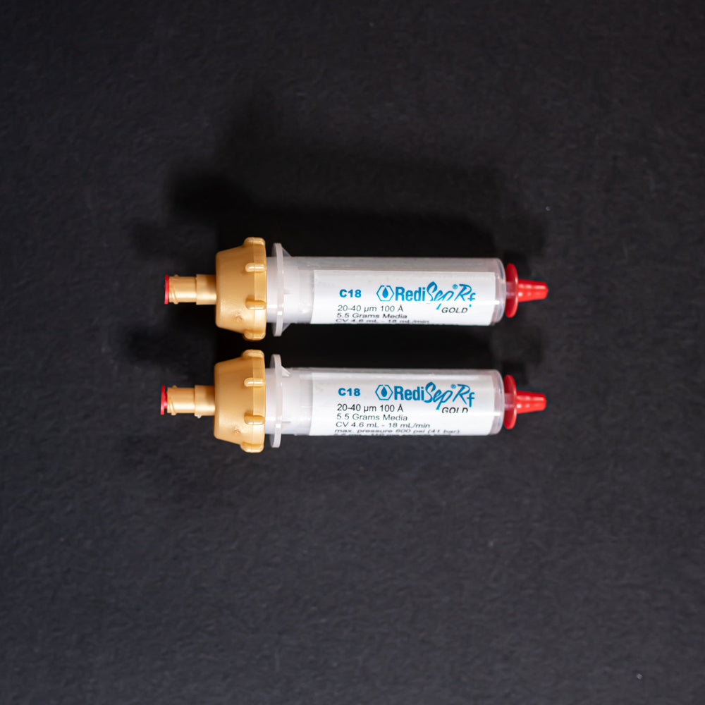 A pair of small white tubes with gold and red caps displayed on a black background, creating a striking visual contrast between the two elements.