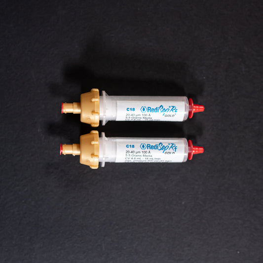 A pair of small white tubes with gold and red caps displayed on a black background, creating a striking visual contrast between the two elements.