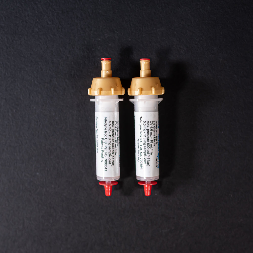 A pair of small white tubes with gold and red caps displayed on a black background, creating a striking visual contrast between the two elements.