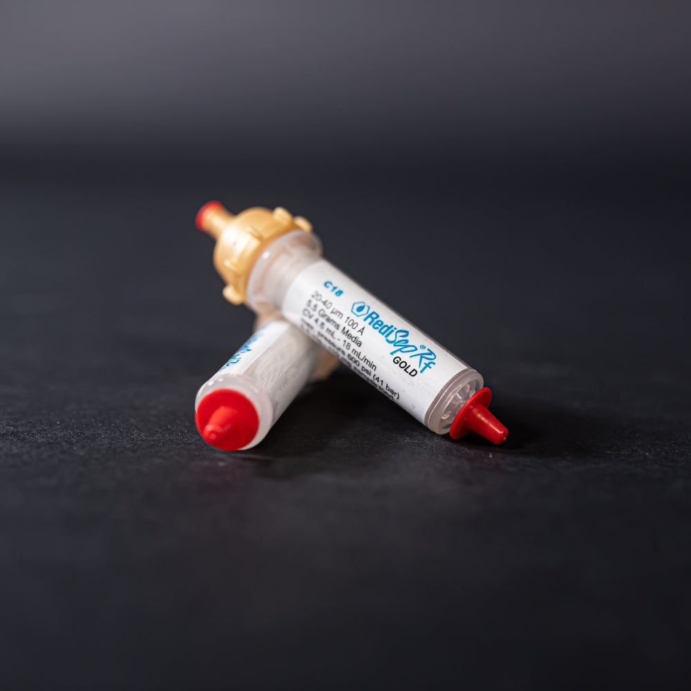A pair of small white tubes with gold and red caps displayed on a black background, creating a striking visual contrast between the two elements.