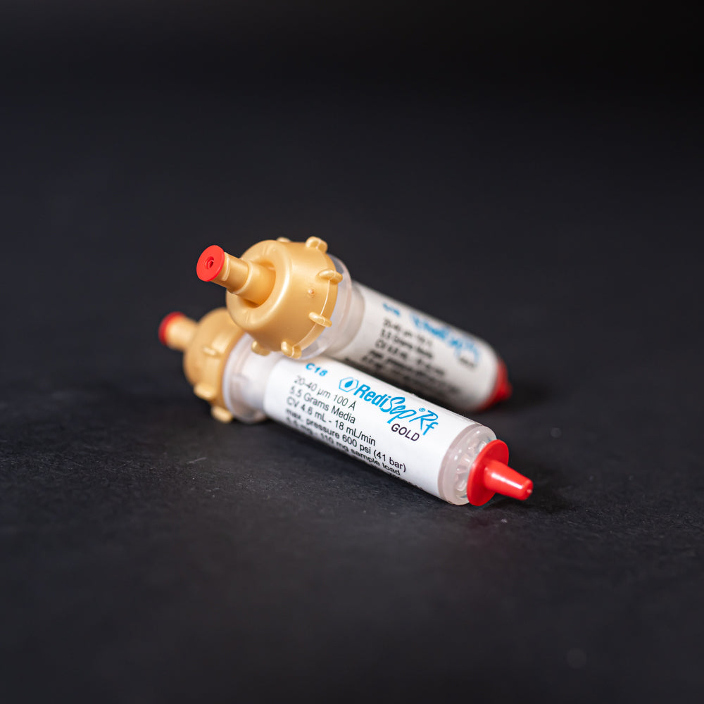 A pair of small white tubes with gold and red caps displayed on a black background, creating a striking visual contrast between the two elements.