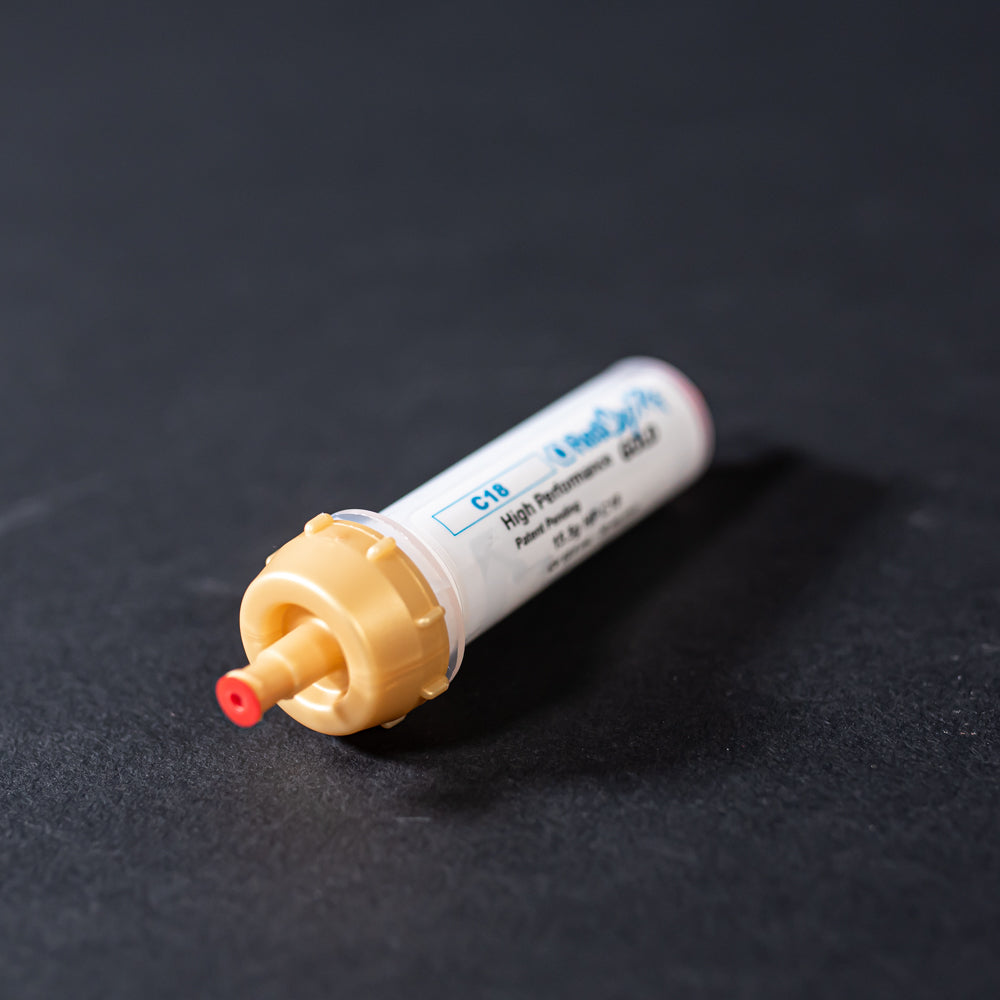 A small white tube with gold and red caps displayed on a black background, creating a striking visual contrast between the two elements.