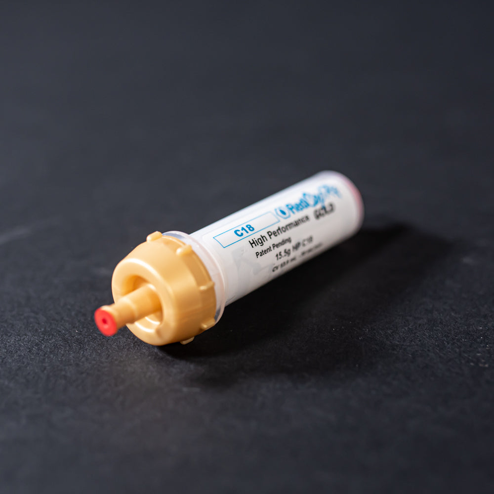 A small white tube with gold and red caps displayed on a black background, creating a striking visual contrast between the two elements.