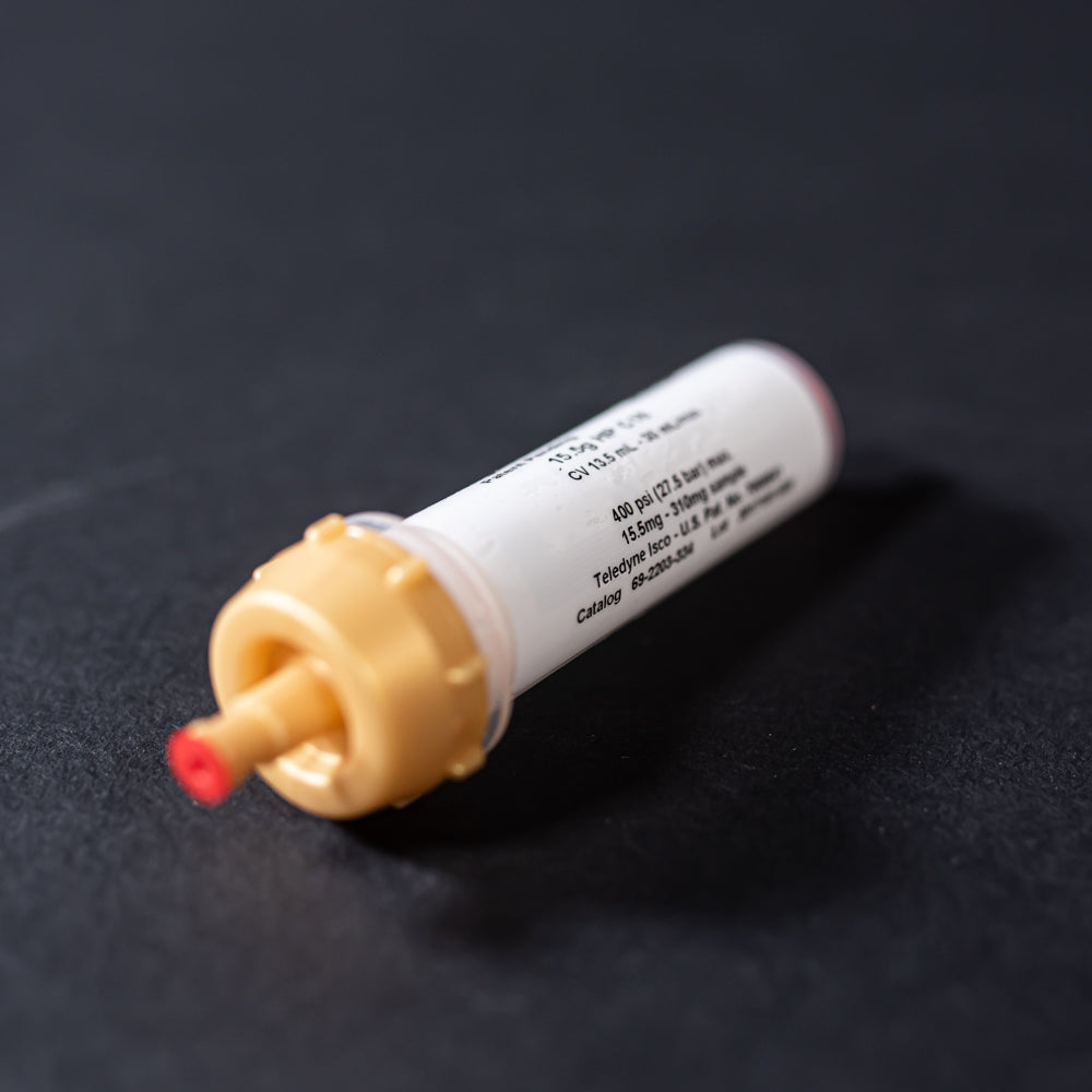 A small white tube with gold and red caps displayed on a black background, creating a striking visual contrast between the two elements.