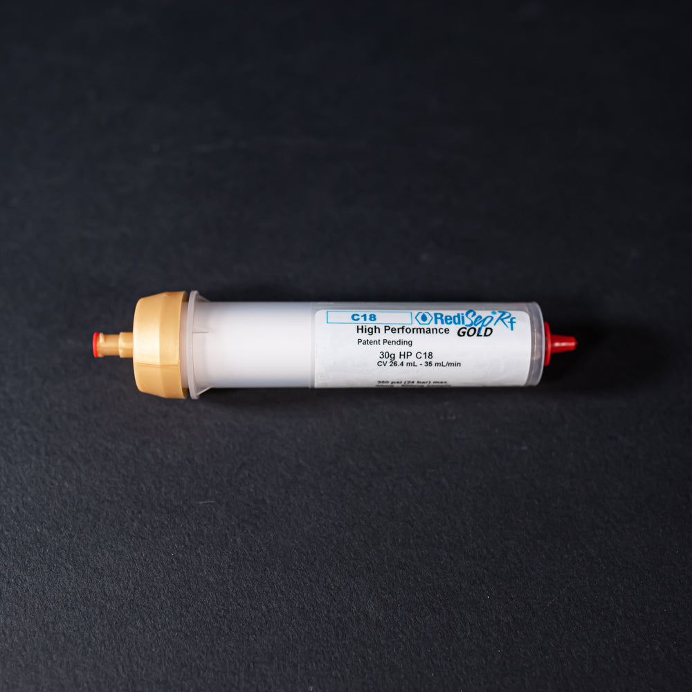 A small white tube with gold and red caps displayed on a black background, creating a striking visual contrast between the two elements.