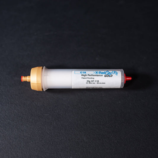 A small white tube with gold and red caps displayed on a black background, creating a striking visual contrast between the two elements.