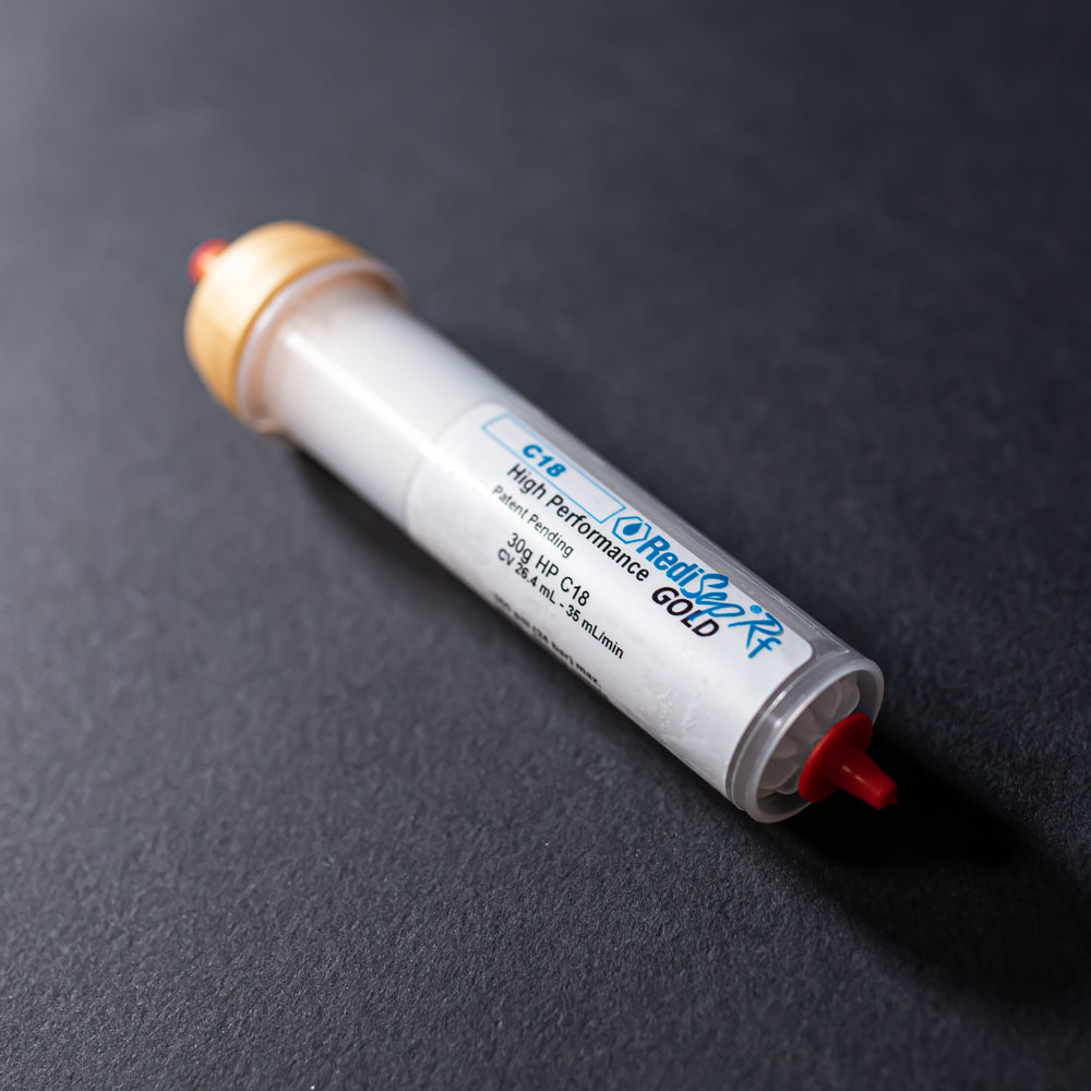 A small white tube with gold and red caps displayed on a black background, creating a striking visual contrast between the two elements.