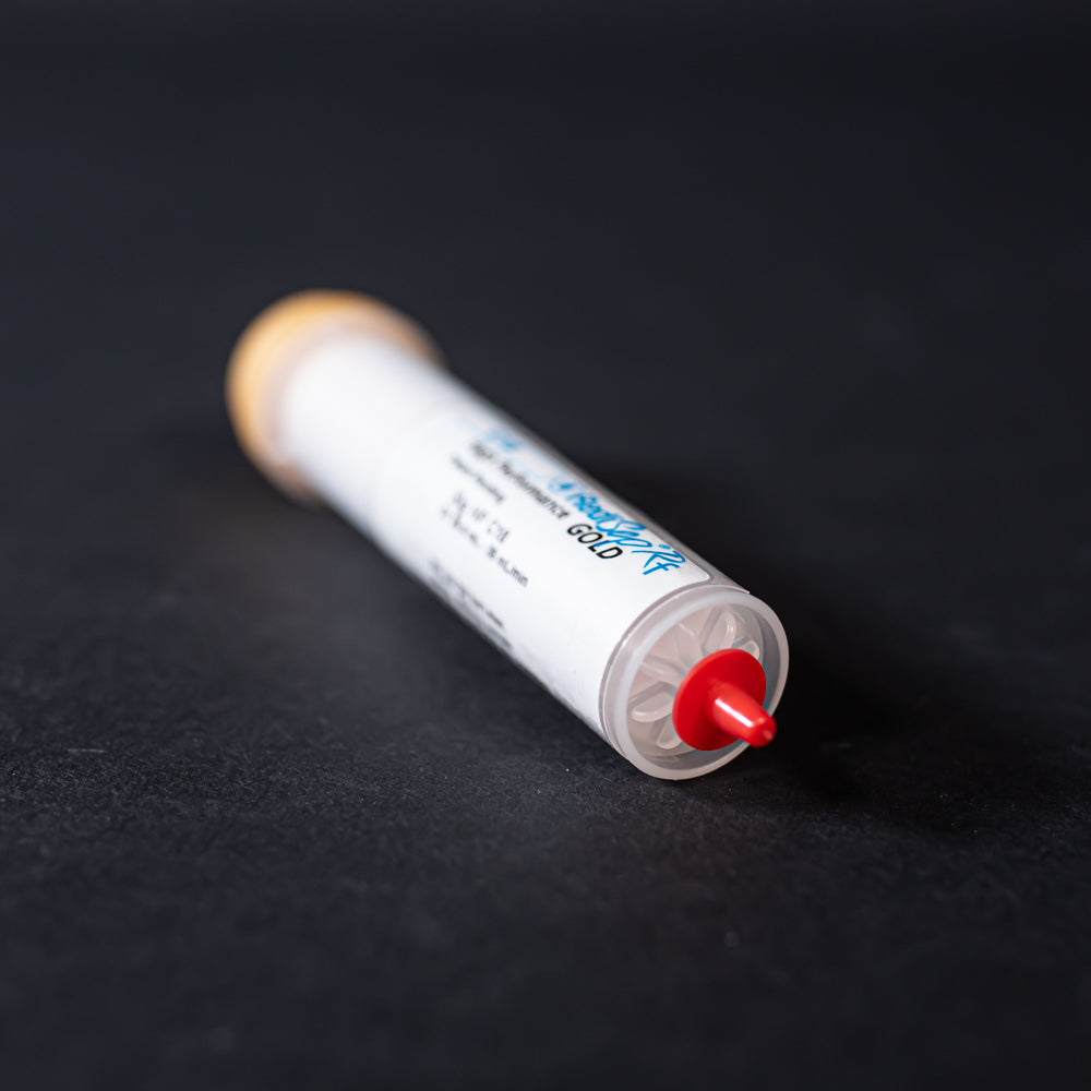 A small white tube with gold and red caps displayed on a black background, creating a striking visual contrast between the two elements.