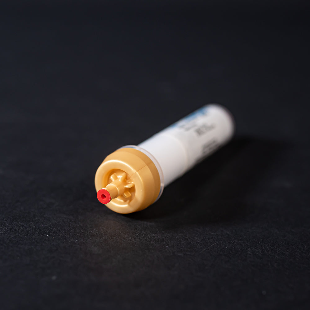 A small white tube with gold and red caps displayed on a black background, creating a striking visual contrast between the two elements.
