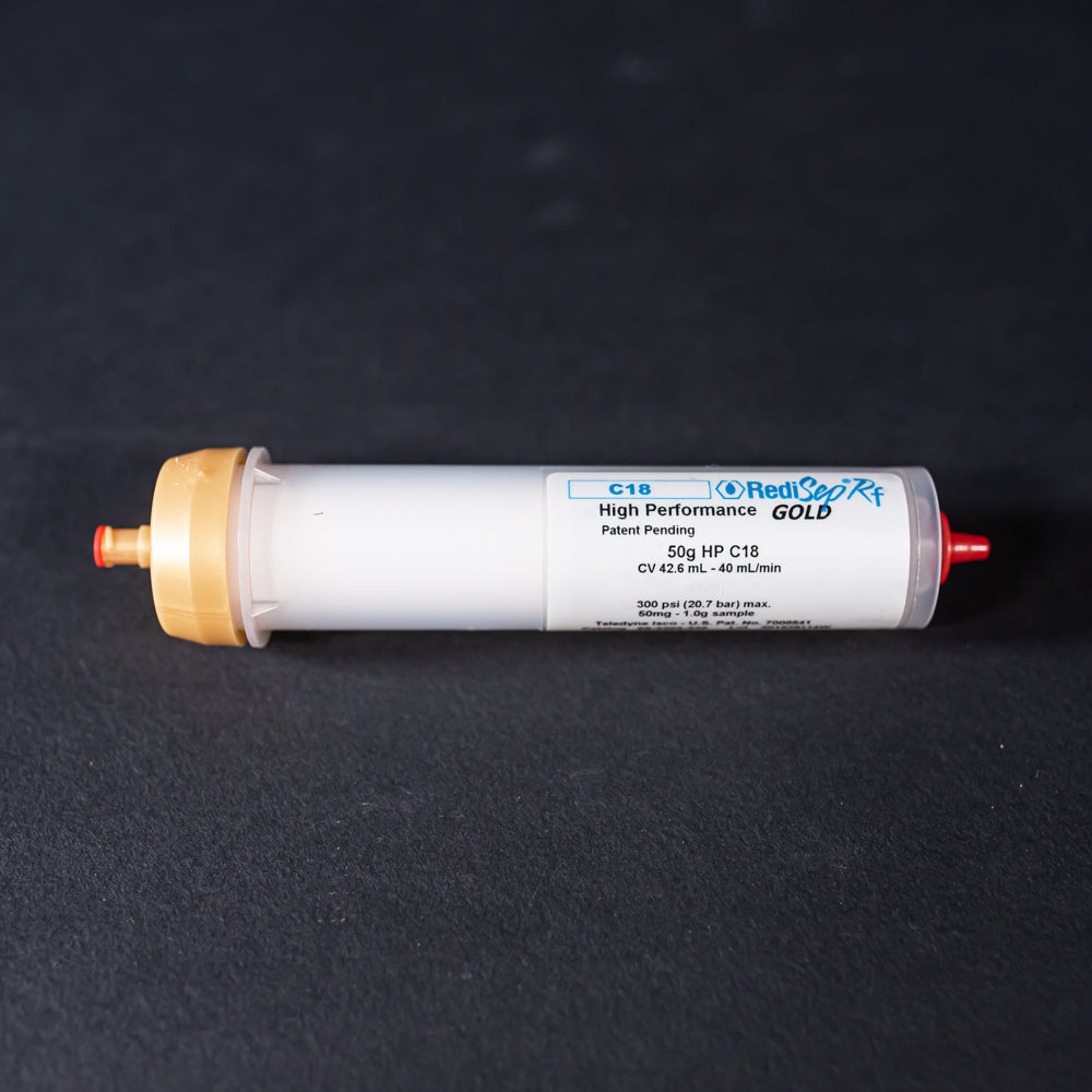 A small white tube with gold and red caps displayed on a black background, creating a striking visual contrast between the two elements.