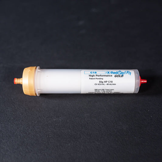 A small white tube with gold and red caps displayed on a black background, creating a striking visual contrast between the two elements.