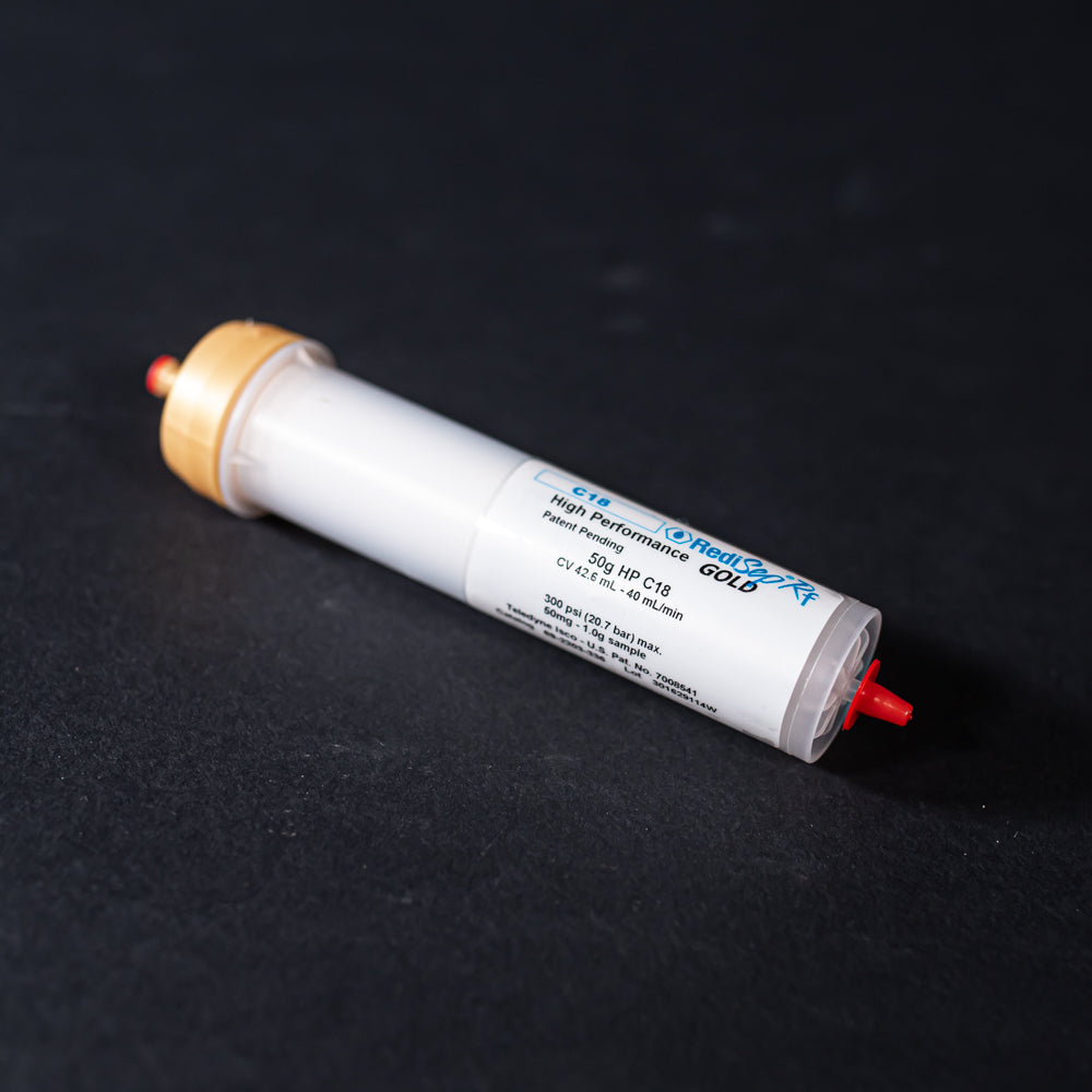 A small white tube with gold and red caps displayed on a black background, creating a striking visual contrast between the two elements.