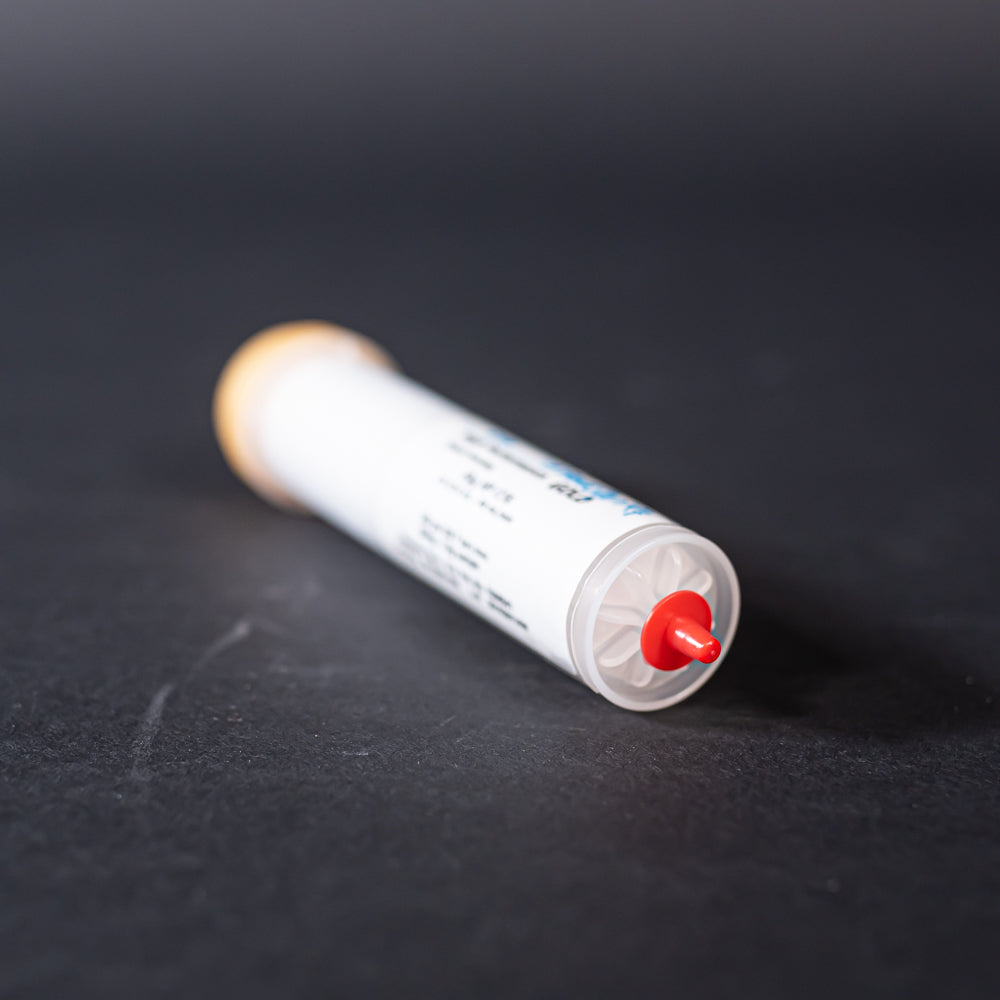 A small white tube with gold and red caps displayed on a black background, creating a striking visual contrast between the two elements.