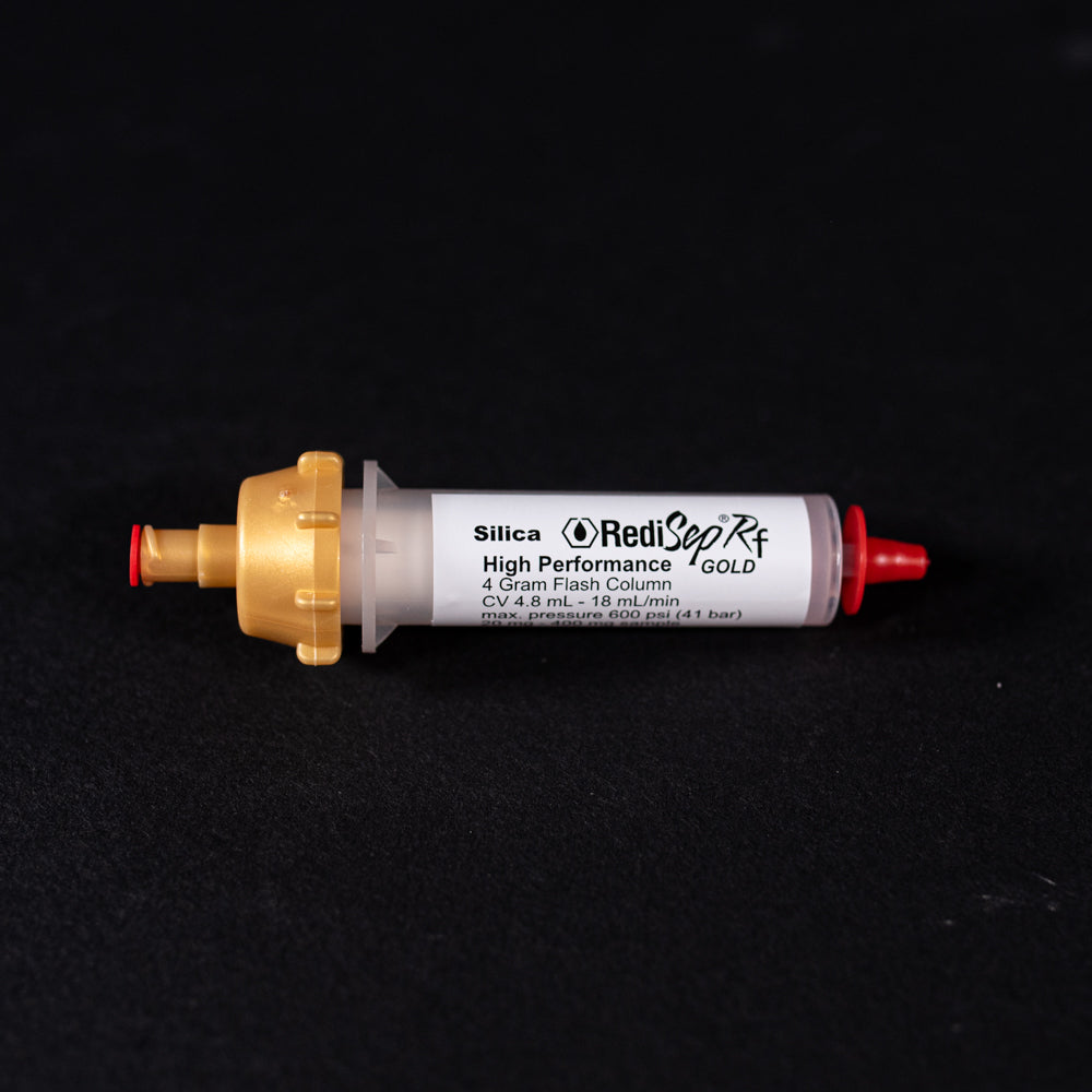A small white tube with gold and red caps displayed on a black background, creating a striking visual contrast between the two elements.