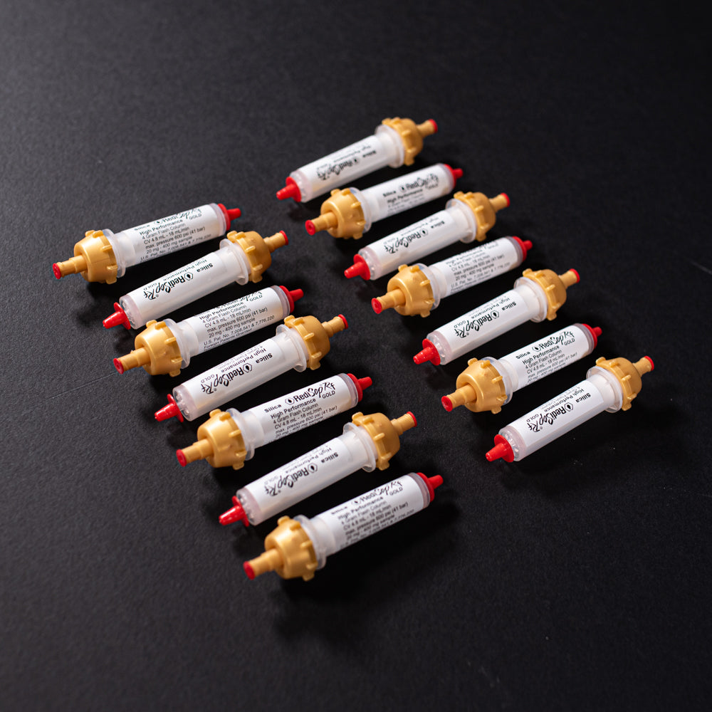 A group of small white tubes with gold and red caps displayed on a black background, creating a striking visual contrast between the two elements.