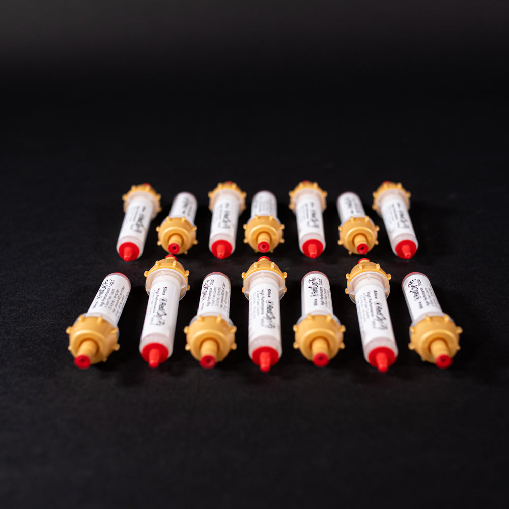 A group of small white tubes with gold and red caps displayed on a black background, creating a striking visual contrast between the two elements.