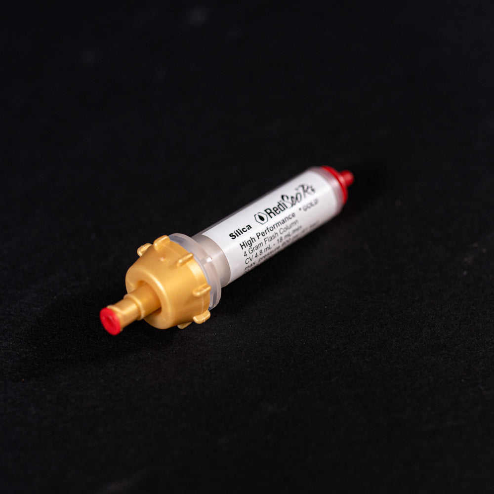 A small white tube with gold and red caps displayed on a black background, creating a striking visual contrast between the two elements.