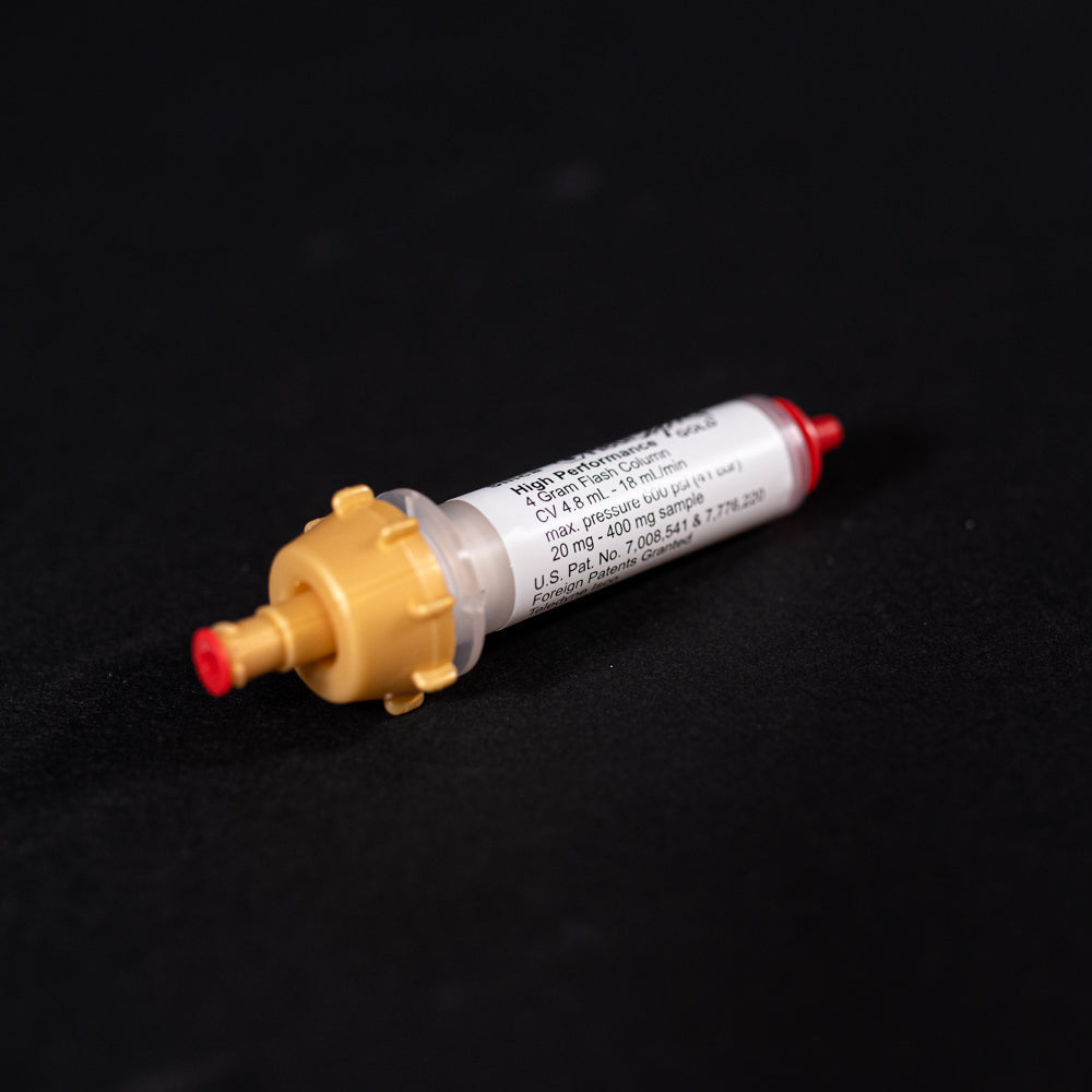 A small white tube with gold and red caps displayed on a black background, creating a striking visual contrast between the two elements.