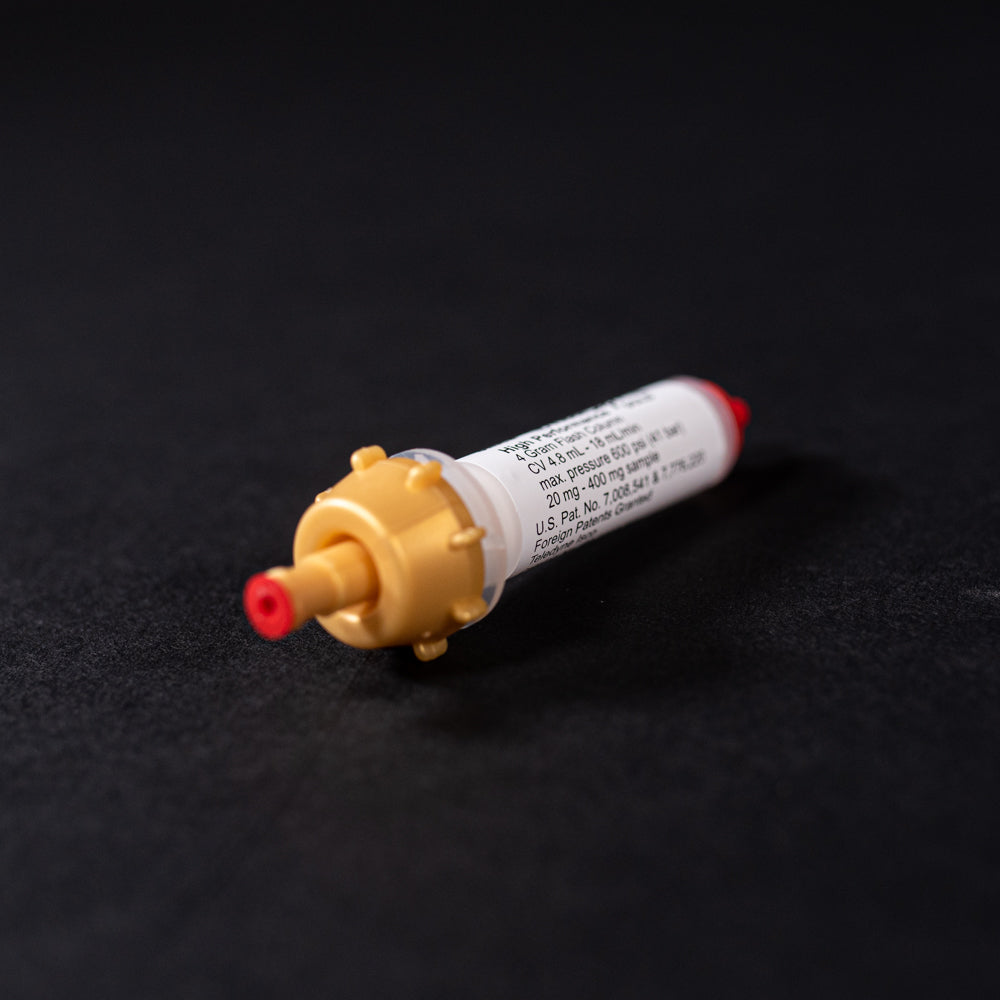 A small white tube with gold and red caps displayed on a black background, creating a striking visual contrast between the two elements.