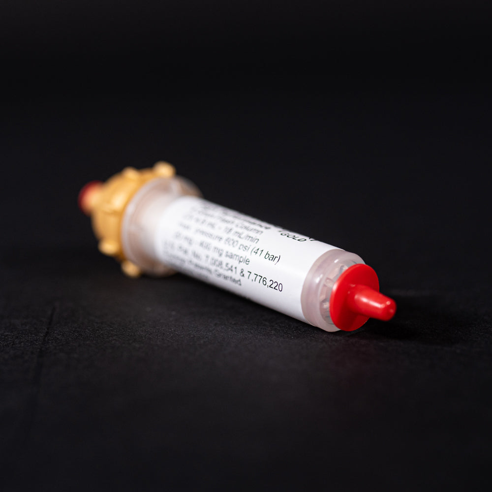 A small white tube with gold and red caps displayed on a black background, creating a striking visual contrast between the two elements.