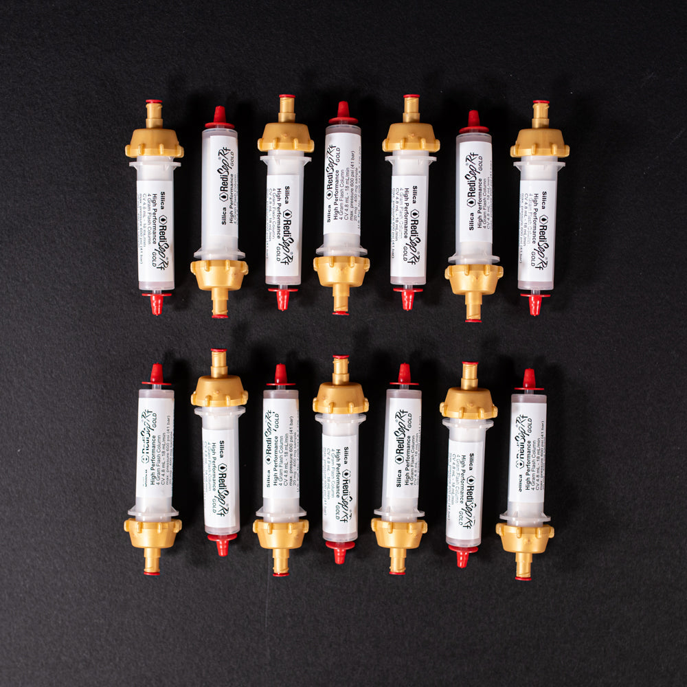 A group of small white tubes with gold and red caps displayed on a black background, creating a striking visual contrast between the two elements.