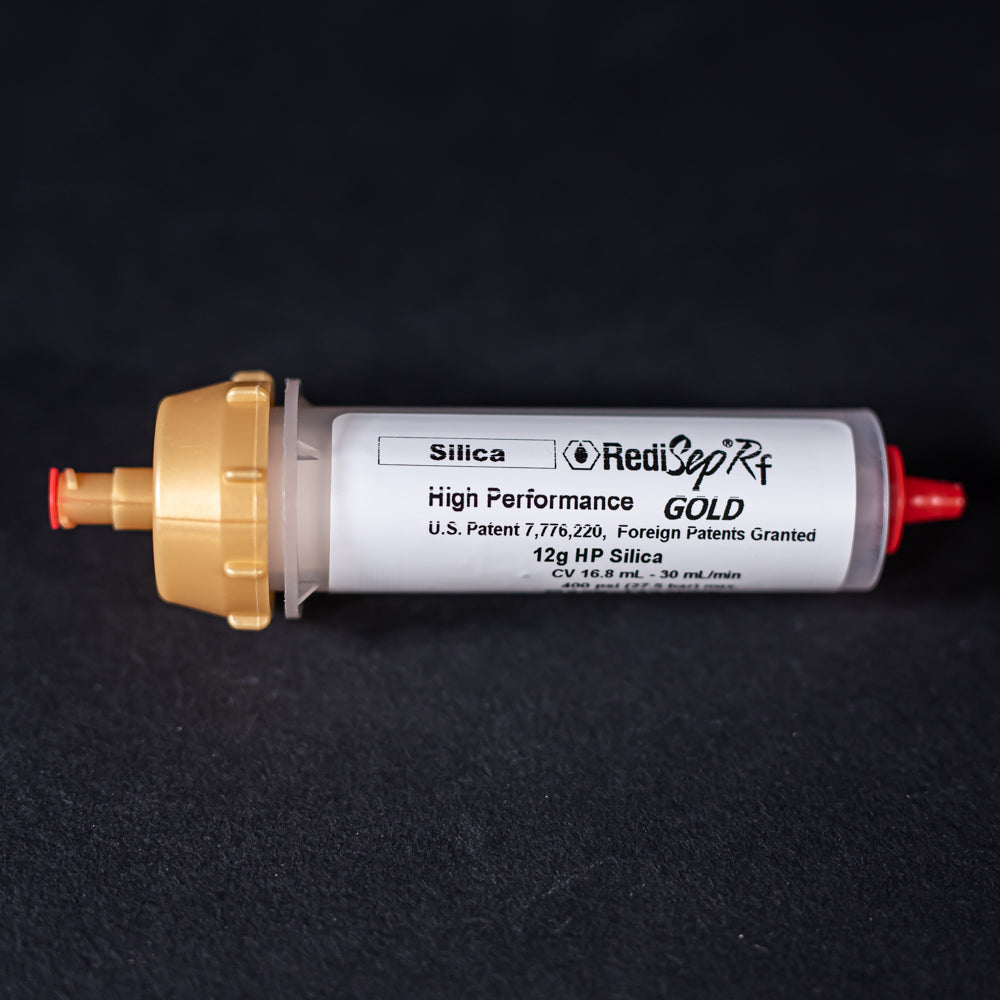 A small white tube with gold and red caps displayed on a black background, creating a striking visual contrast between the two elements.