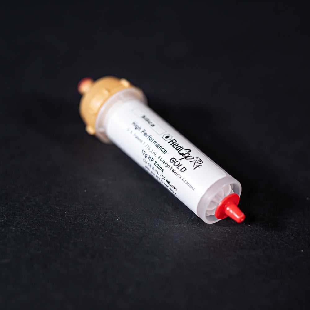 A small white tube with gold and red caps displayed on a black background, creating a striking visual contrast between the two elements.