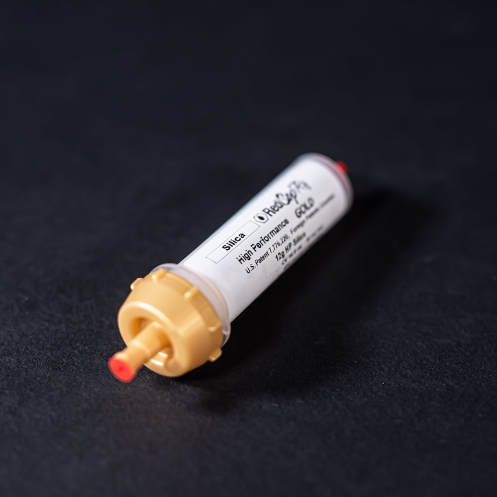 A small white tube with gold and red caps displayed on a black background, creating a striking visual contrast between the two elements.