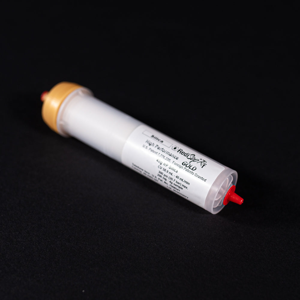 A small white tube with gold and red caps displayed on a black background, creating a striking visual contrast between the two elements.