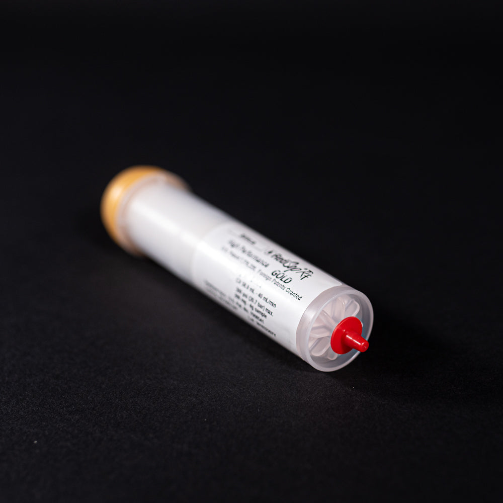 A small white tube with gold and red caps displayed on a black background, creating a striking visual contrast between the two elements.