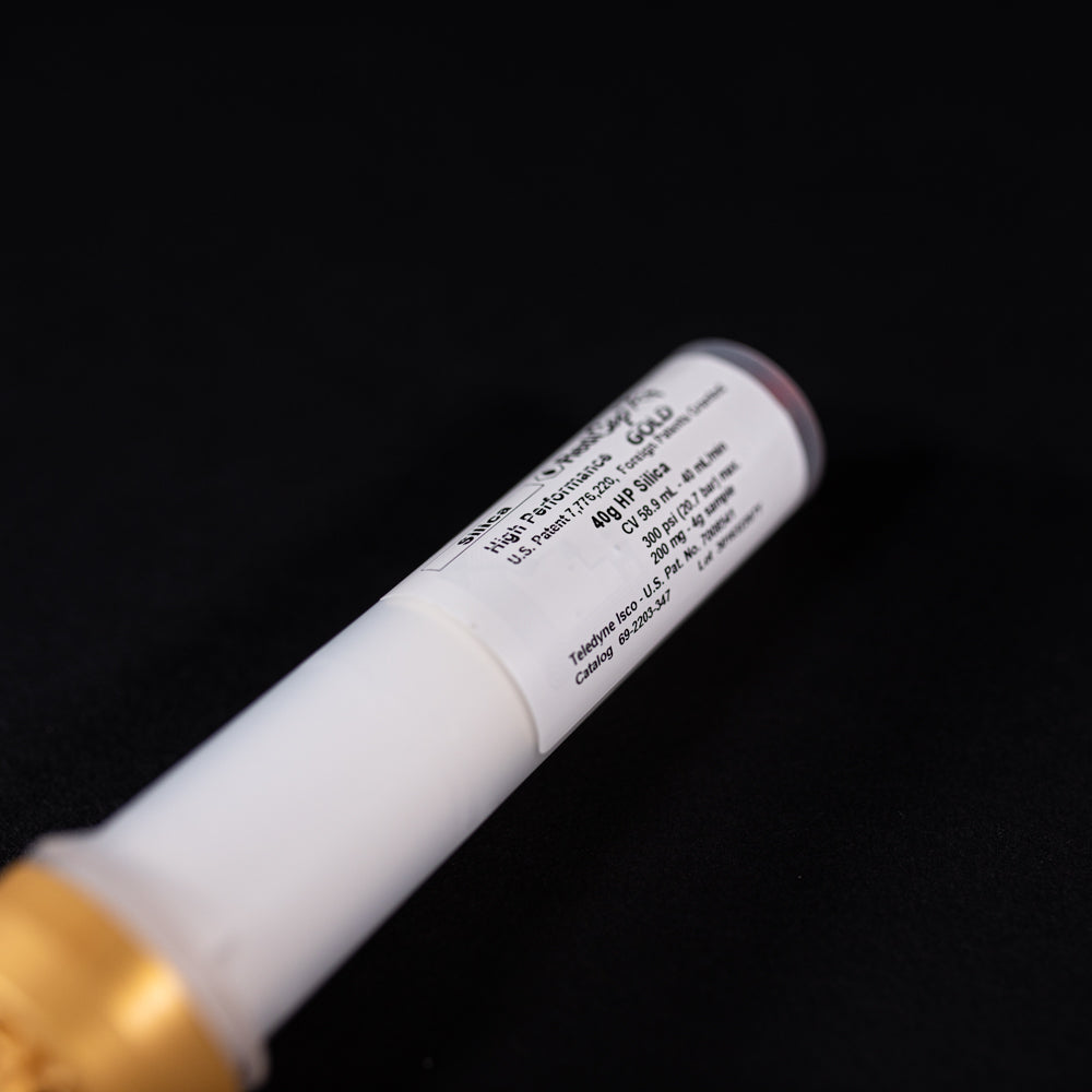 A small white tube with gold and red caps displayed on a black background, creating a striking visual contrast between the two elements.
