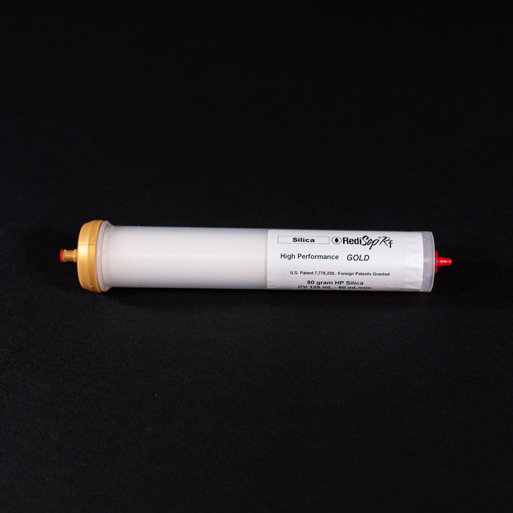 A small white tube with gold and red caps displayed on a black background, creating a striking visual contrast between the two elements.