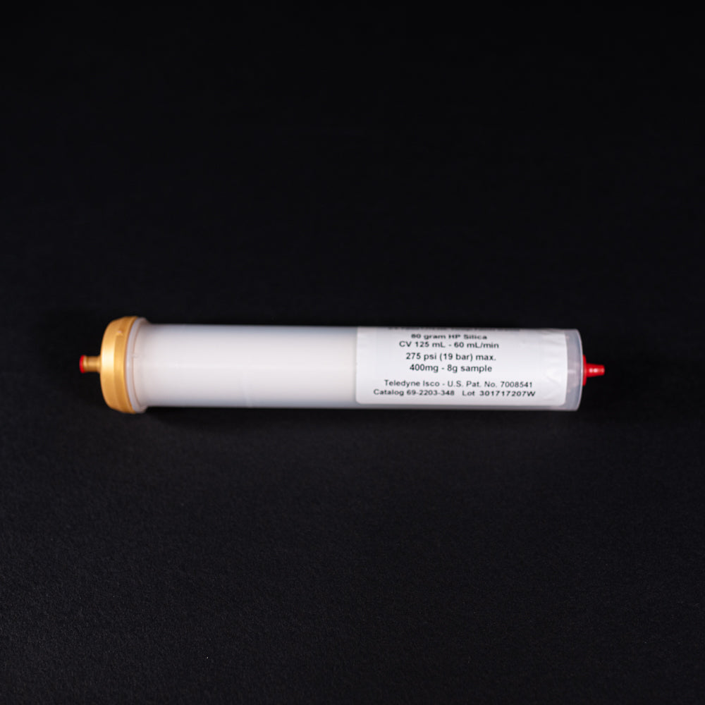 A small white tube with gold and red caps displayed on a black background, creating a striking visual contrast between the two elements.