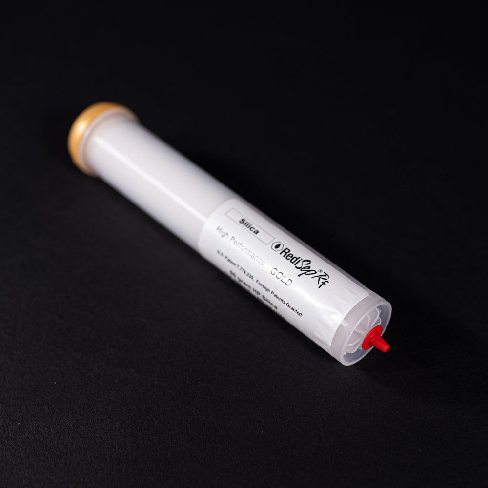 A small white tube with gold and red caps displayed on a black background, creating a striking visual contrast between the two elements.