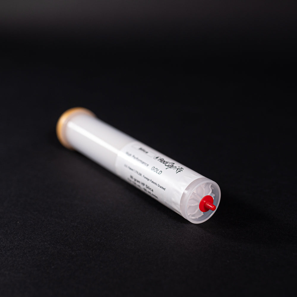 A small white tube with gold and red caps displayed on a black background, creating a striking visual contrast between the two elements.