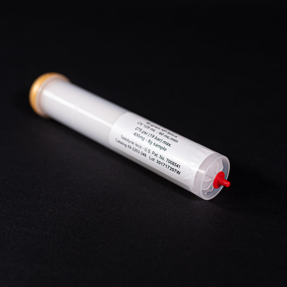 A small white tube with gold and red caps displayed on a black background, creating a striking visual contrast between the two elements.