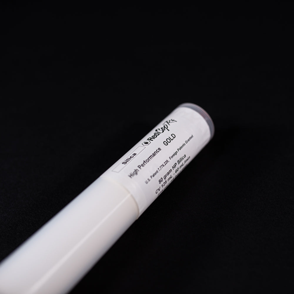 A small white tube with gold and red caps displayed on a black background, creating a striking visual contrast between the two elements.