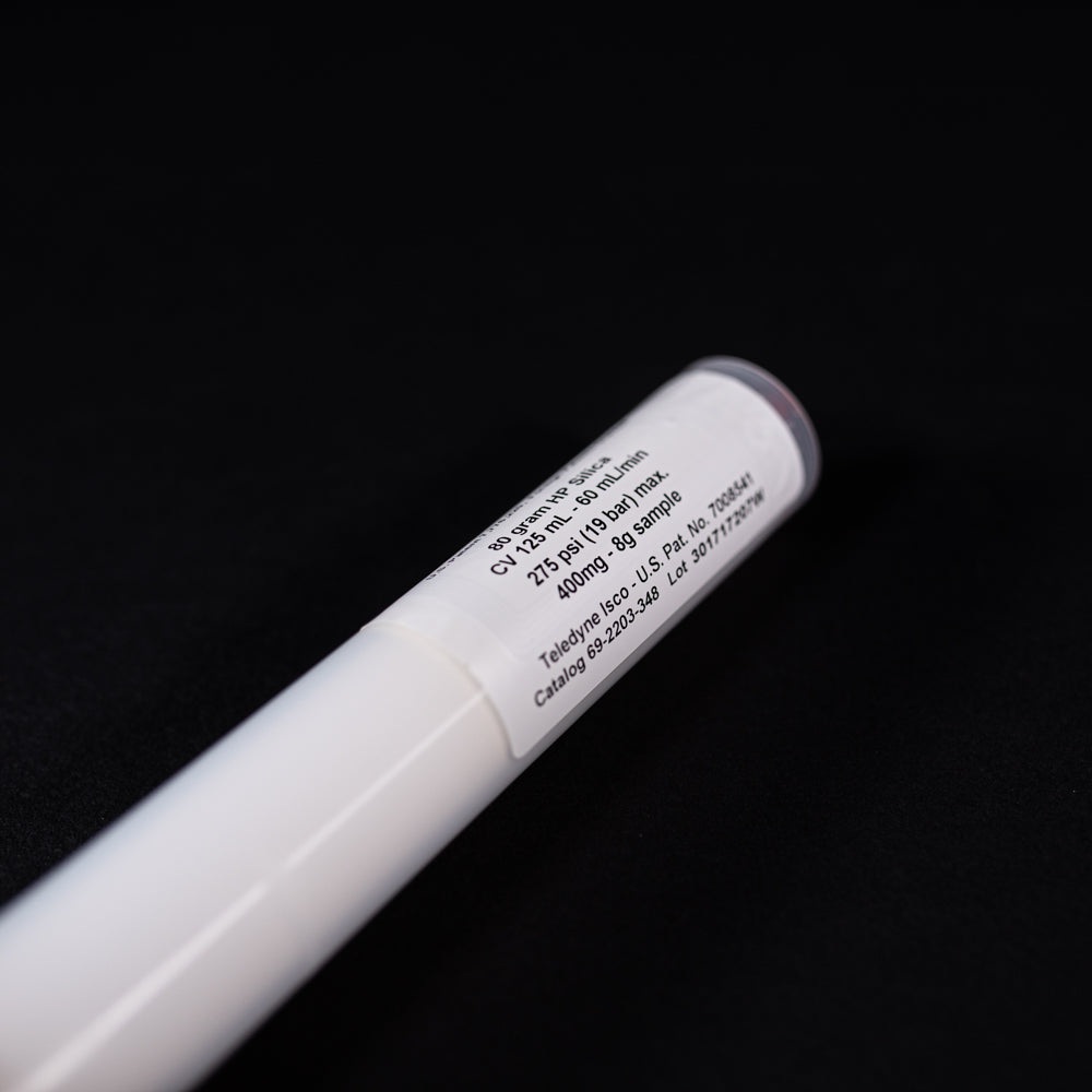 A small white tube with gold and red caps displayed on a black background, creating a striking visual contrast between the two elements.