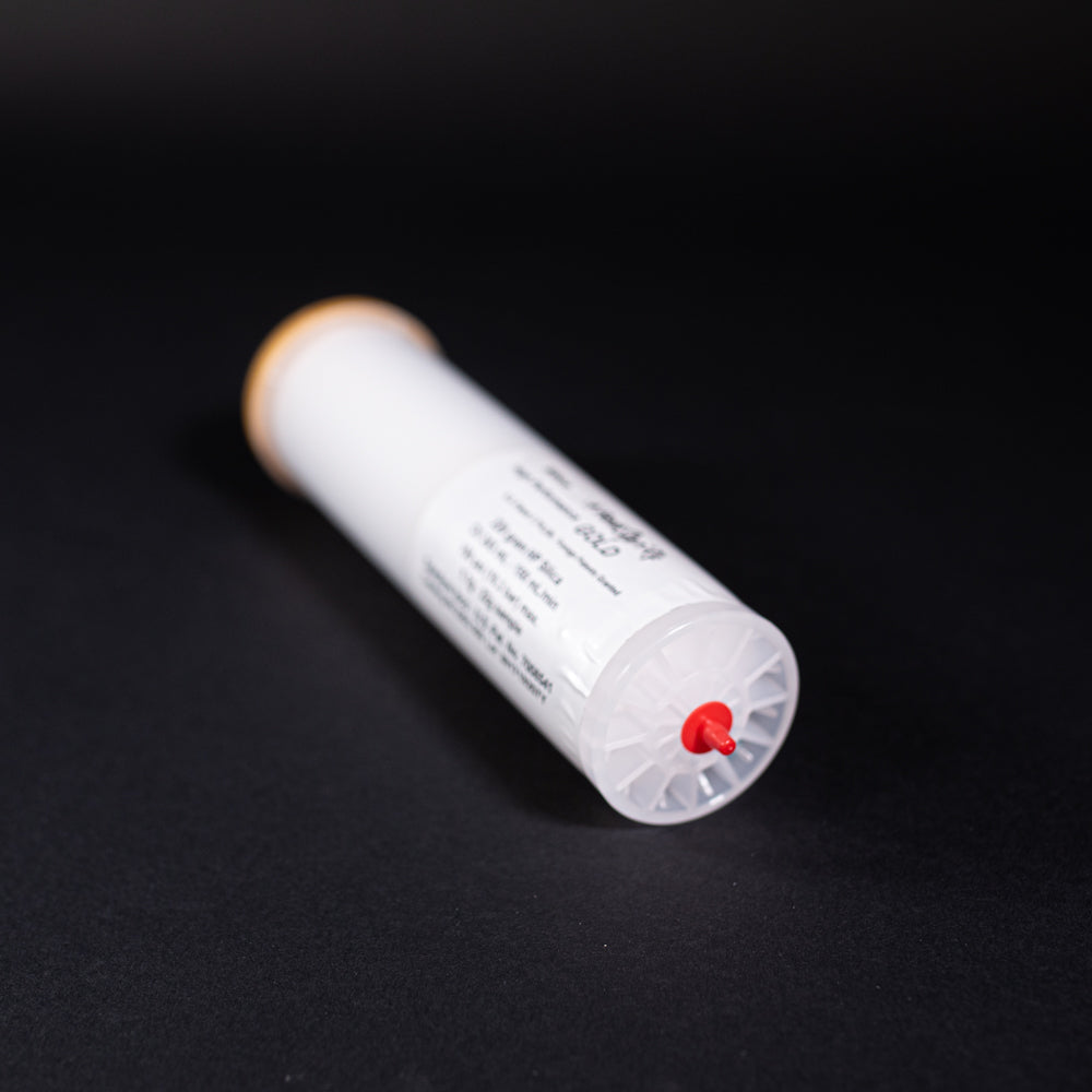 A small white tube with gold and red caps displayed on a black background, creating a striking visual contrast between the two elements.