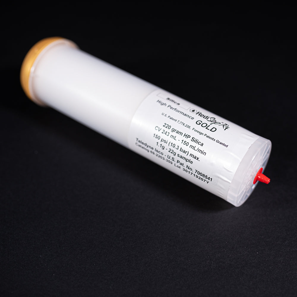 A small white tube with gold and red caps displayed on a black background, creating a striking visual contrast between the two elements.