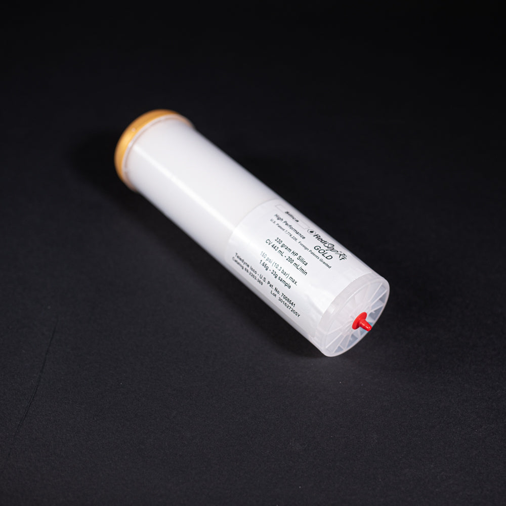A small white tube with gold and red caps displayed on a black background, creating a striking visual contrast between the two elements.