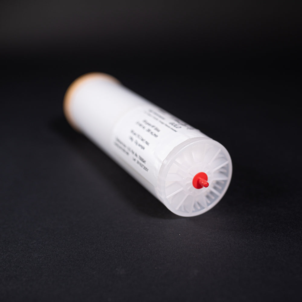 A small white tube with gold and red caps displayed on a black background, creating a striking visual contrast between the two elements.