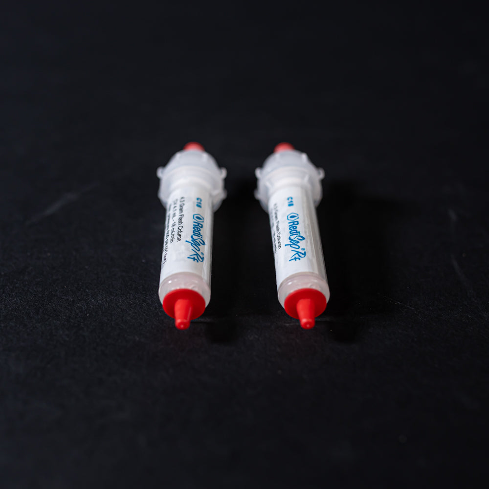A pair of small white tubes with red caps displayed on a black background, creating a striking visual contrast between the two elements.