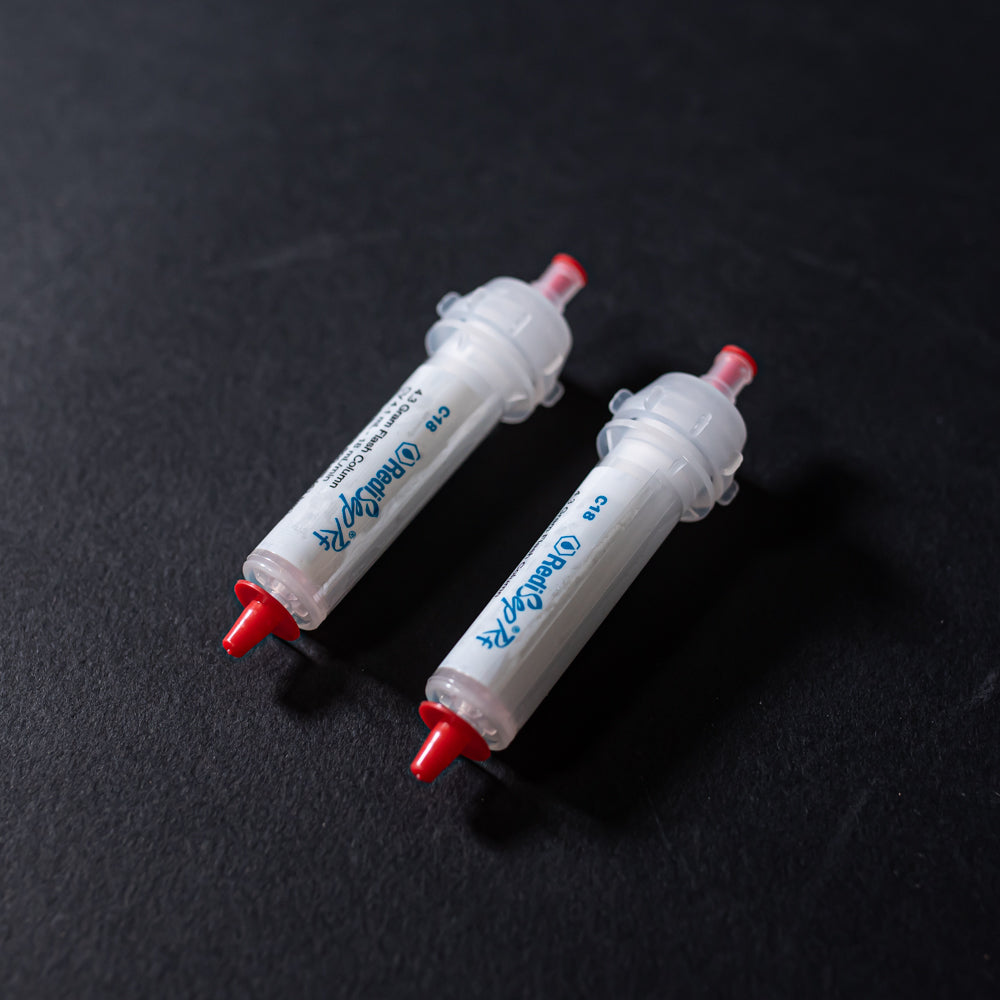 A pair of small white tubes with red caps displayed on a black background, creating a striking visual contrast between the two elements.