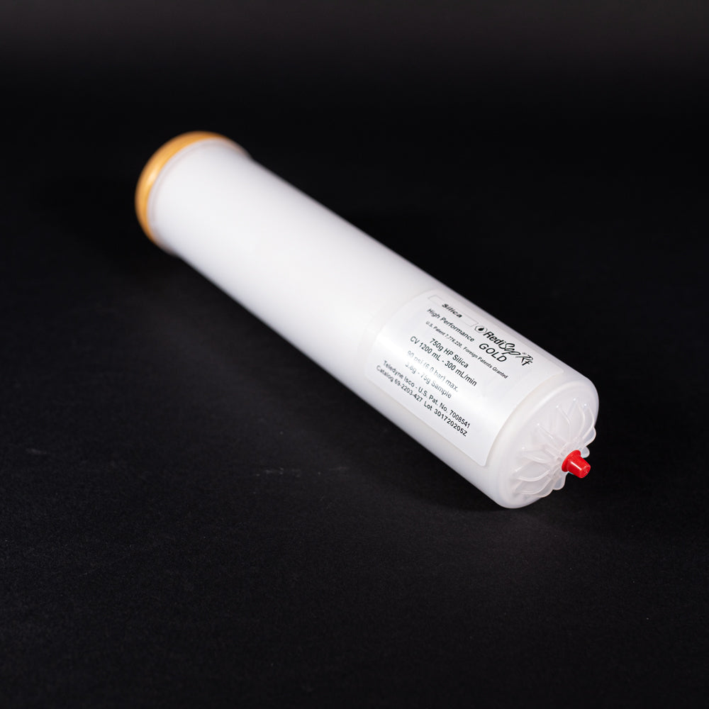 A small white tube with gold and red caps displayed on a black background, creating a striking visual contrast between the two elements.