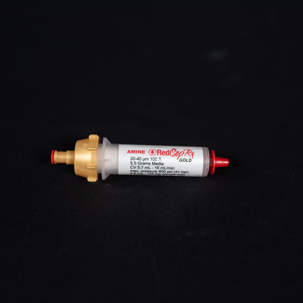 A small white tube with gold and red caps displayed on a black background, creating a striking visual contrast between the two elements.